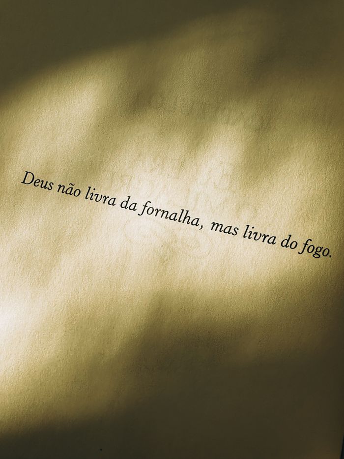 the-story Quote 'Deus não livra da fornalha, mas livra do fogo' on textured paper with light shadows.