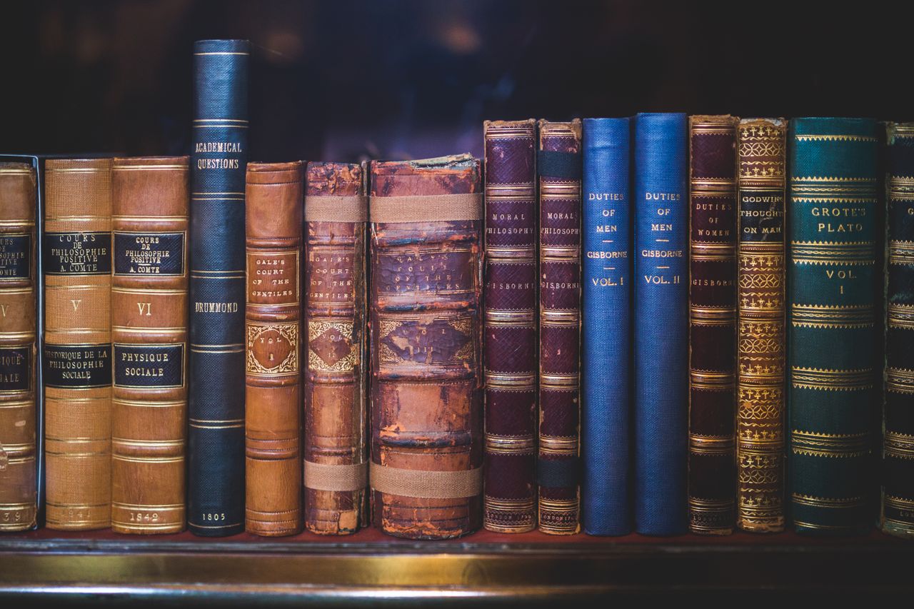our-mission A collection of classic, leather-bound books neatly arranged on a wooden bookshelf.